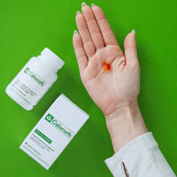 Hand holding Calocurb Amarasate appetite control capsules with supplement bottle and box on a vibrant green background for weight management and craving support.