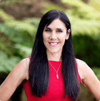 Lisa Tamati, genetics and functional-health practitioner, smiling outdoors in a red top with native bush behind her