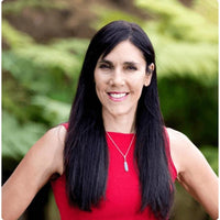 Lisa Tamati, genetics and functional-health practitioner, smiling outdoors in a red top with native bush behind her